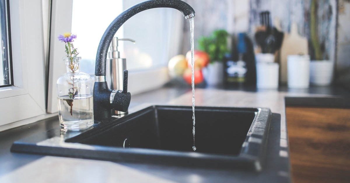 Zwarte keukenkraan laat water in een donkere spoelbak stromen