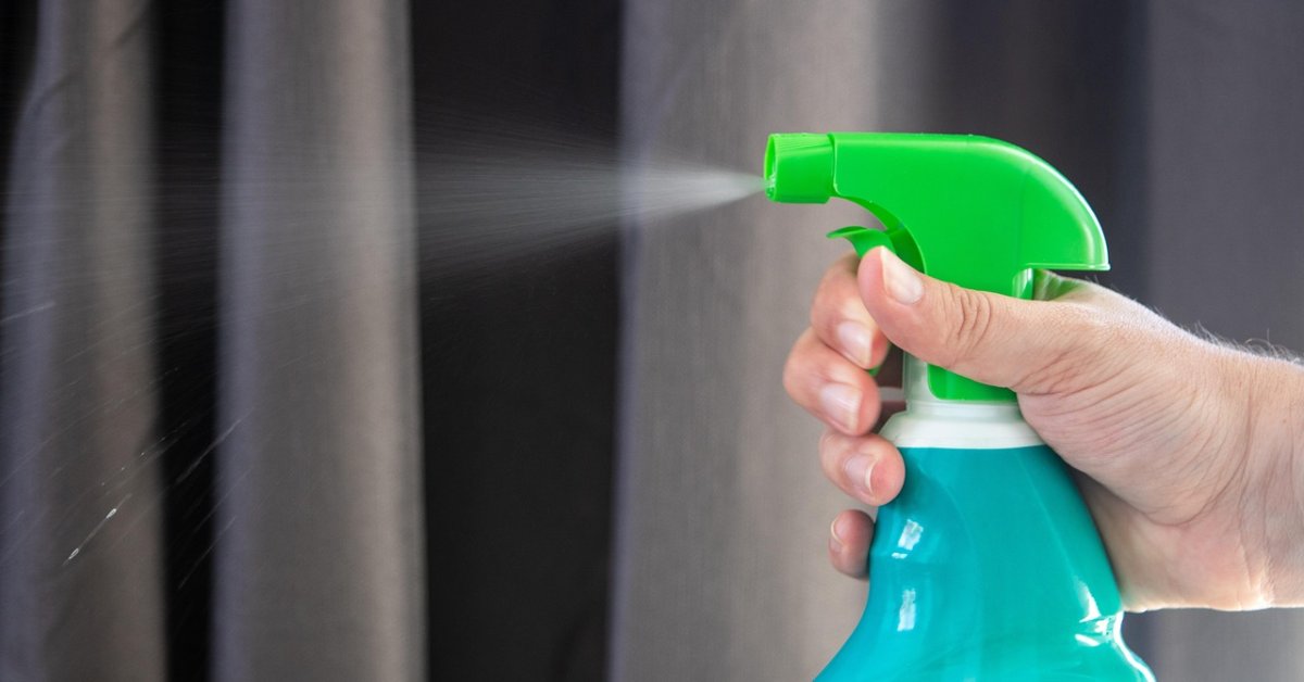 Hand sprayt met een turquoise schoonmaakfles op een gordijn