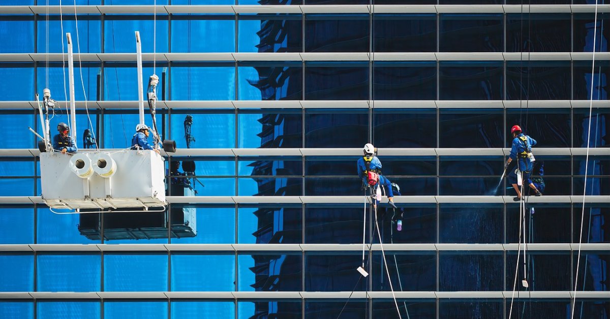 Glazenwassers reinigen hangend aan touwen de gevel van een glazen kantoorgebouw